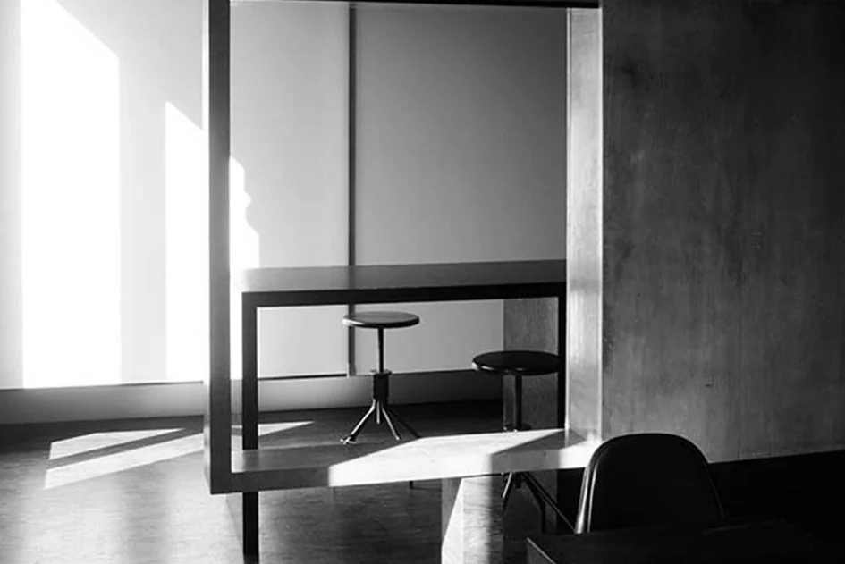 Brutalist office with a long raw concrete work surface, wooden floor and slanted glass wall
